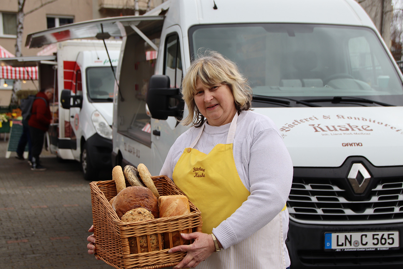 Eine Verkäuferin mit einem Korb voll verschiedenem Brot vor dem Wagen von Bäckerei Kuske